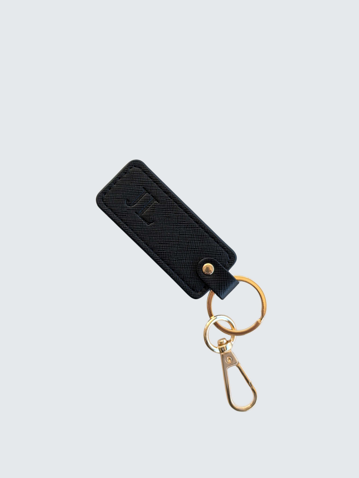 A black textured leather keychain with an embossed monogram, attached to gold-tone metal key rings and a lobster clasp, shown on a light gray background.